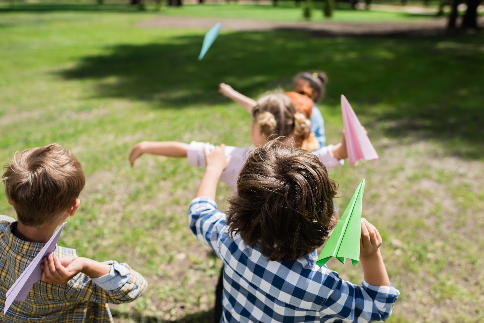 cute little children throwing paper planes in park